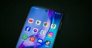 Close-up of a smartphone screen showing colorful app icons (YouTube, Play Store, Chrome, Maps, Facebook, Instagram, WhatsApp, Pinterest, Discord, TikTok) on a dark background.