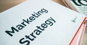 downloaded-image - Local SEO and Search Engine Marketing | FMS Online Marketing Close-up of a white folder with bold black text reading 'Marketing Strategy' and an orange spine on the right edge of the desk surface.