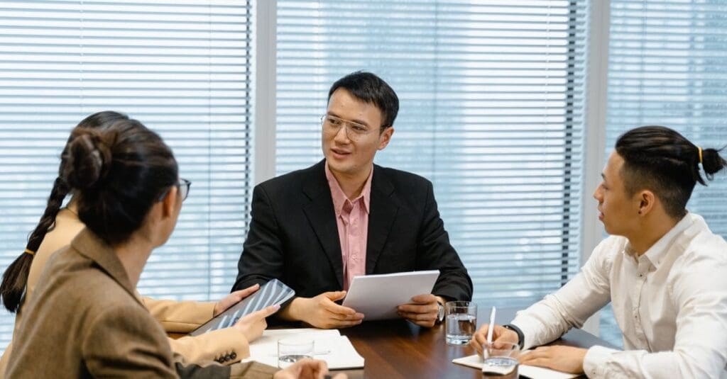 Group of four professionals in a meeting around a wooden table, discussing documents and notes.