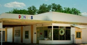 Colorful donut shop storefront with a large glass display and a rainbow 'DONUTS' sign on the roofline.