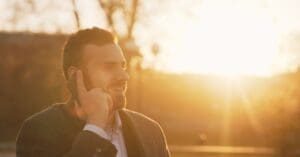 Man in a blazer talking on his smartphone outdoors during sunset, smiling to the side in warm golden light